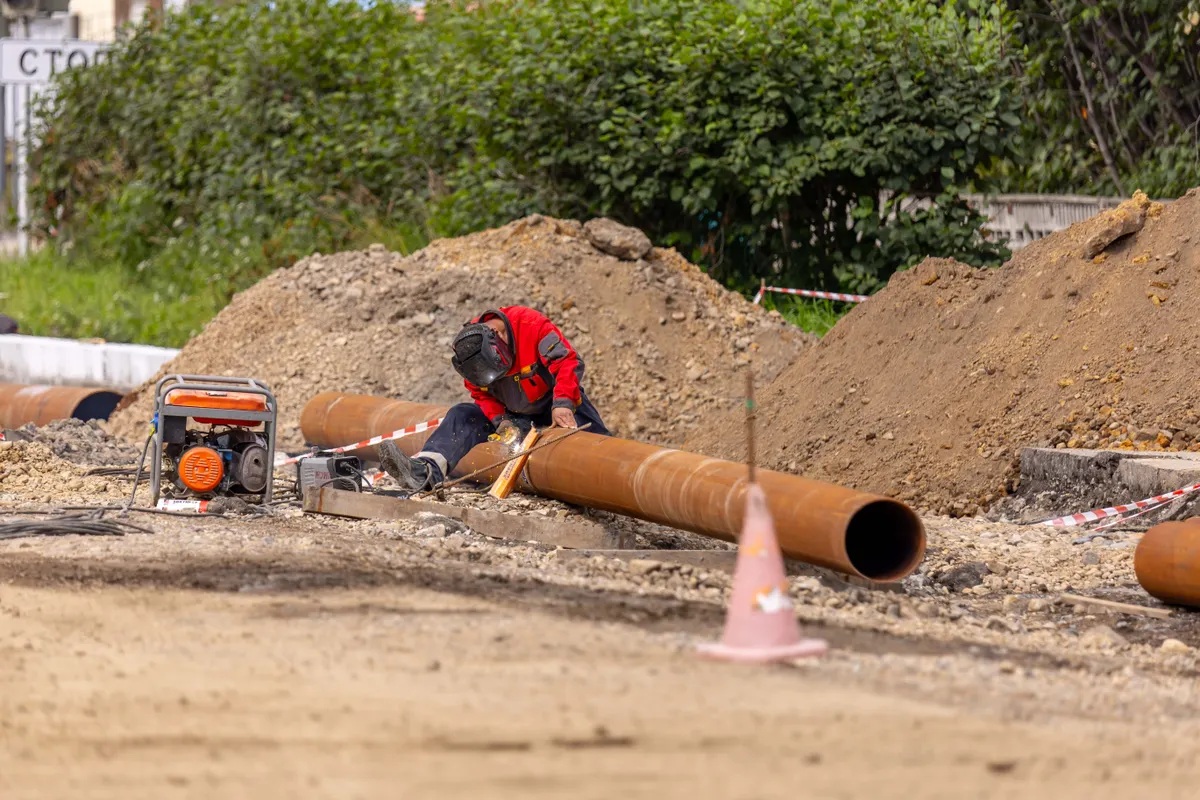 Sewer Line Repair Gilroy CA — worker welding a large pipe at an outdoor excavation site