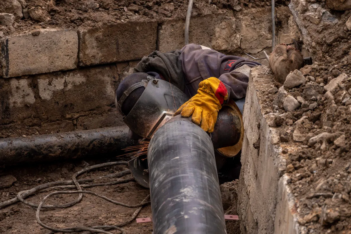 Emergency Sewer Line Repair Kirkland WA — worker welding a pipe in an urban trench